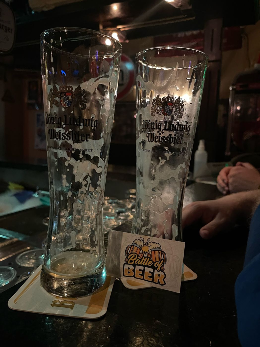 Zwei geleerte Weizengläser mit Battle-of-Beer-Kärtchen auf dem Tresen